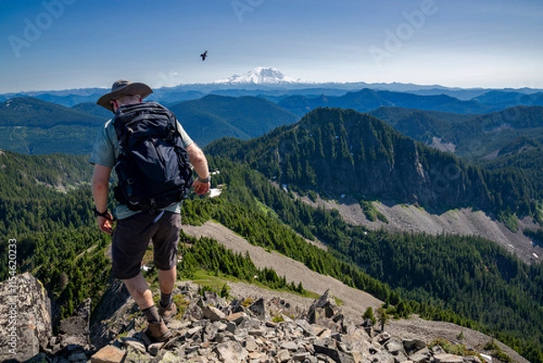 Fototapeta Athletic adventurous male hiker, hiking down a ridge on top of a mountain with Mount Rainier in the background during a beautiful sunny day. 