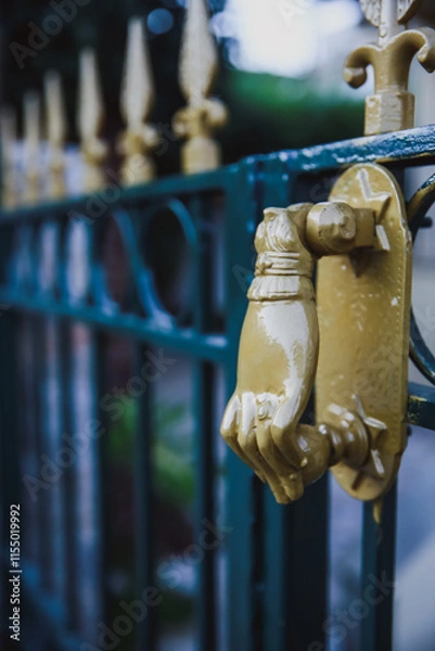 Fototapeta A detailed close-up of a golden door knocker in the shape of a hand, attached to an ornate green gate.