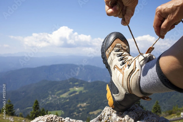 Fototapeta Hiker tying boot laces on rock, high in the mountains, space for text
