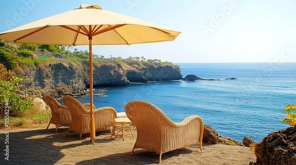 Fototapeta Serene coastal view with wicker chairs under a beach umbrella, overlooking the ocean. Perfect for relaxation and vacation imagery.