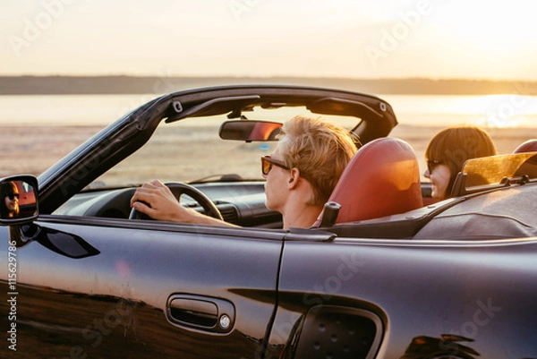 Fototapeta young happy couple in cabriolet in sunset light