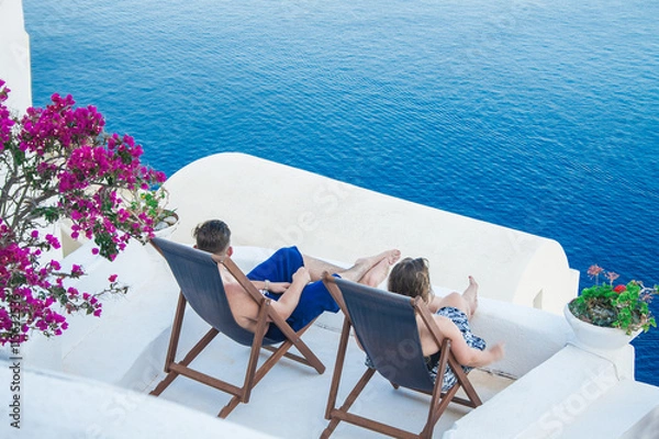 Fototapeta Enjoying the big blue- Young couple enjoying the blue sea on Santorini island, Greece from their hotel balcony.