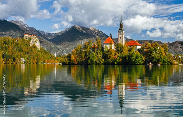 Obraz Lake Bled on a sunny autumn day. A view of the island and the Church of the Assumption of Mary. Traveling through Europe, Slovenia. A forest on the cliffs on a sunny day. Tourist attractions of Europe
