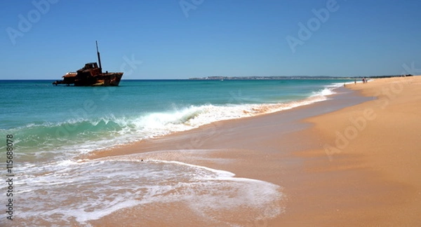 Fototapeta Horizontal landscape of the beach with a fisherman, shipwreck in the background on a sunny day (Stockton Beach, NSW, Australia)