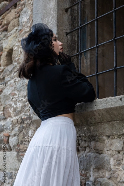 Obraz Young woman with black hair, dressed in black Gothic style, in a dilapidated church with barred windows.