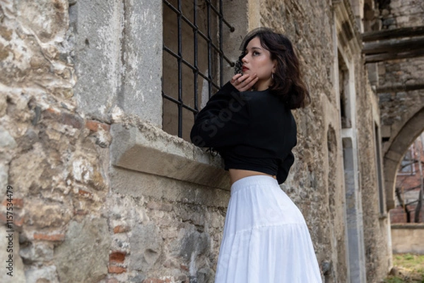 Obraz Young woman with black hair, dressed in black Gothic style, in a dilapidated church with barred windows.