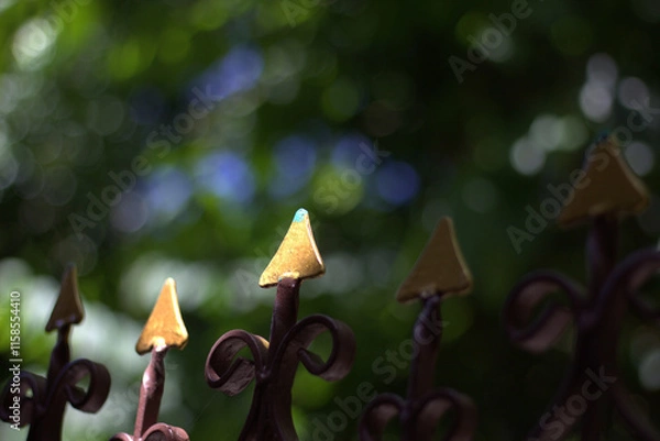 Fototapeta Elegant metal fence with golden tips against blurred green background, creating serene atmosphere. intricate design adds touch of artistry to scene