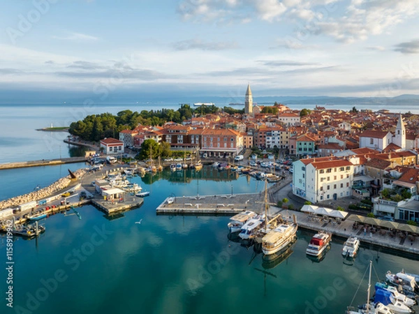 Fototapeta Aerial panoramic view of picturesque Izola town with the old town and buildings with red roofs, the main promenade, the marina with boats on Adriatic sea coast, Slovenia.