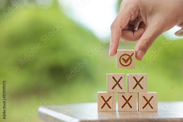 Fototapeta One hand holds a wooden block with the correct.mark and X on it. These blocks are stacked on top of each other.