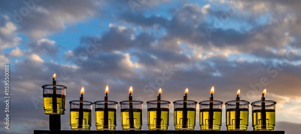 Fototapeta Hanukkah design. Image depicts Jewish Holiday of Miracle Light – Hanukkah, selected focus on menorah with olive oil burning candles, blurred cloud  background. No AI tools were used
