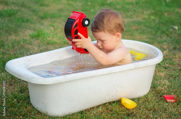 Fototapeta A small baby bathed in the bath and playing with toy car.