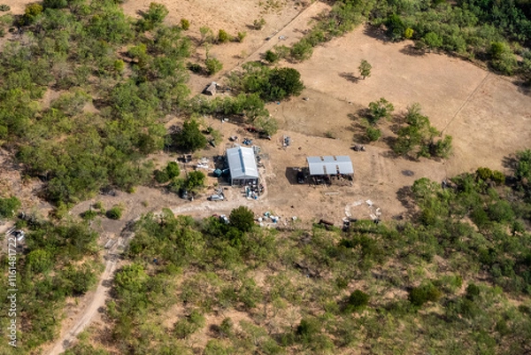 Fototapeta Austin, Texas - Aerial view of a car port and storage shed on the outskirts of Austin Texas with an abandoned car and debris strewn around the yard and open field in the hill country scrub brush