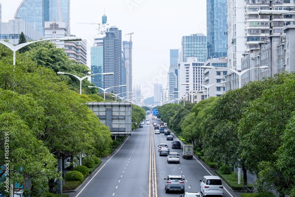 Fototapeta Elevated view of a modern urban boulevard in Xiamen, China, featuring a well-planned cityscape with green tree-lined streets and contemporary high-rise buildings.