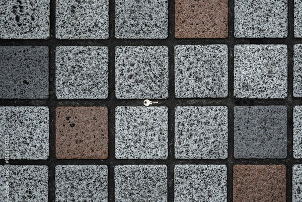 Fototapeta A close-up photo of a small silver key placed on a patterned stone tile surface.