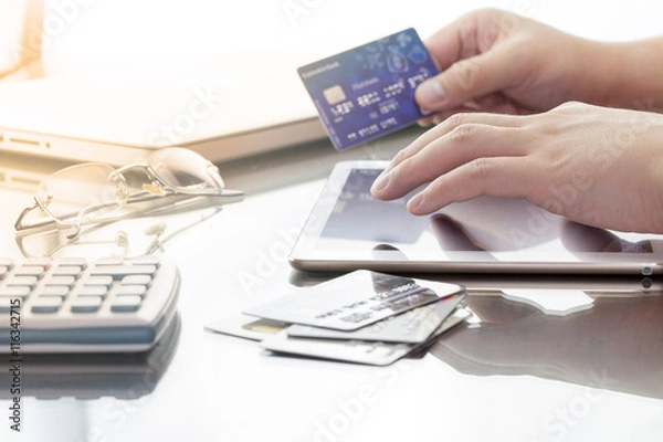 Fototapeta Man using his digital tablet while holding a credit card intent to online shopping, concept with digital business or e-commerce concept. close up, warm tone.