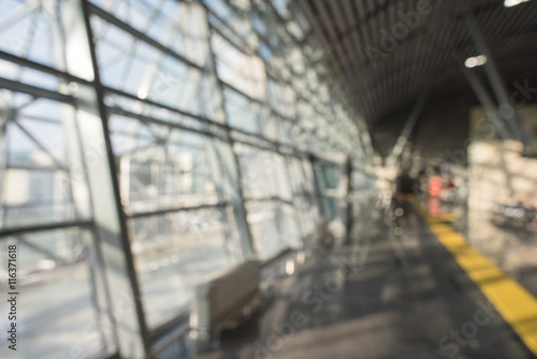 Fototapeta Blurred airport terminal background. Airport or railway hall interior in bokeh. International gate, business trip, arrival or mall. Urban construction.