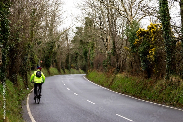 Fototapeta man riding a bicycle up a country road in high-visibility jacket 