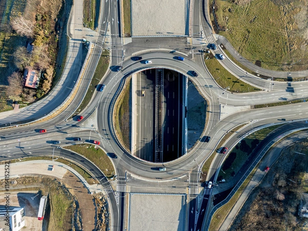 Fototapeta Krakow, Poland. Wegrzce interchange on new S52 highway (below) opened on December 23, 2024. Part of freeway around Cracow. Traffic circle with a hole inside and ramps. Aerial view from above at sunset