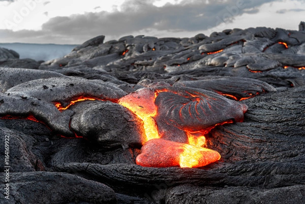 Fototapeta Lava field in Hawaii at dusk shows magma oozing through cracks in the earth and forming what will be new terrain.