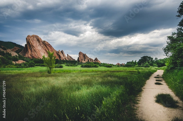 Obraz Landscape of a road passing by a green field with rock formations before a storm.