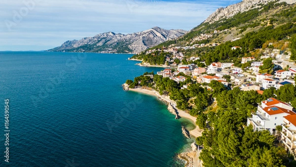 Fototapeta A stunning aerial view of Brela, Croatia, showcasing the iconic Kamen Brela rock formation surrounded by crystal-clear turquoise waters. The coastline is dotted with pristine beaches