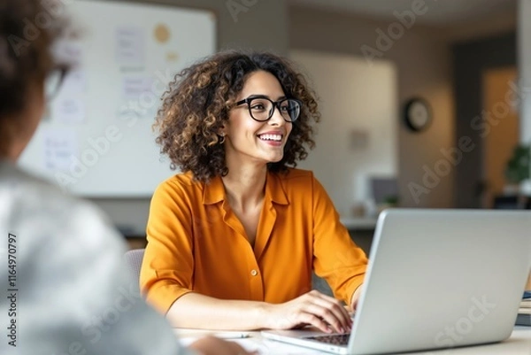 Fototapeta Woman in orange shirt with glasses smiling while working on laptop, modern office background, concept of productivity and workplace positivity. Ai generative