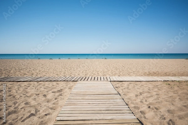 Fototapeta Wooden walkway on the sandy beach of the sea under the blue sky