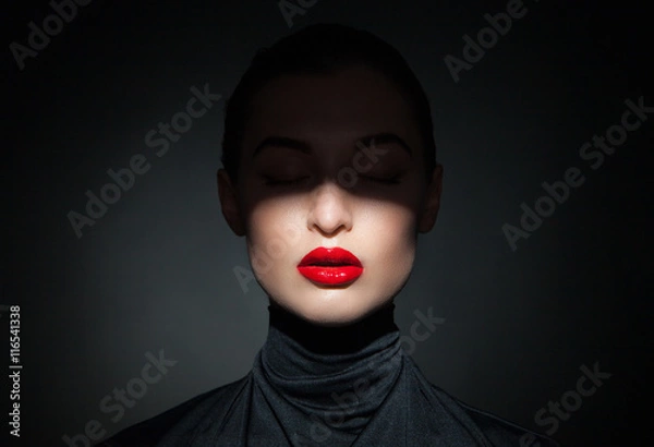Fototapeta Beautiful model with bright red lips and face half covered in shadow