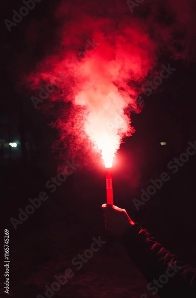 Fototapeta A hand holding a red flare, with smoke in the dark sky