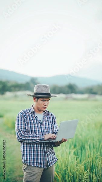 Fototapeta Happy Asian male farmer in the field Wear a hat and carry a smart tablet to track plant growth and disease. The concept of smart farmers using technology