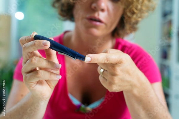 Obraz Close up of a female diabetic patient using lancelet on finger to take sample of blood sugar.