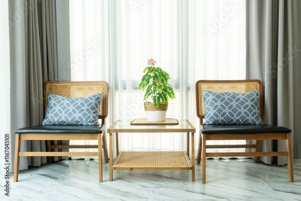 Fototapeta Plants in vase on wooden table and wooden soft chair with decorative cushion. perfect addition to light and airy living room in urban apartment