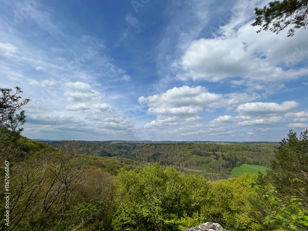 Fototapeta Panoramic view of mountains and trees under blue sky with clouds in the Mullerthal region, Luxembourg.