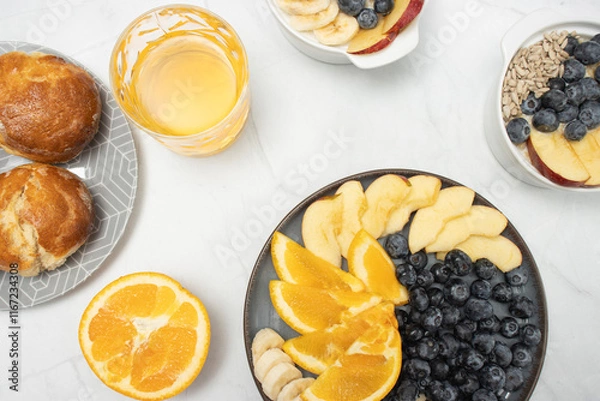 Fototapeta Top view of a breakfast spread featuring fresh fruits, glass of juice, blueberries, orange slices, apple slices, banana, and sunflower seeds, arranged neatly on plates. mindful eating and a balanced d