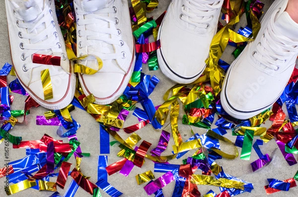 Obraz Two feet in white shoes between multicolored festive confetti on the grey floor
