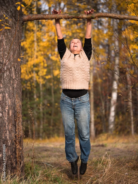 Fototapeta A woman in a sweater and jeans pulled to a branch on blurred background