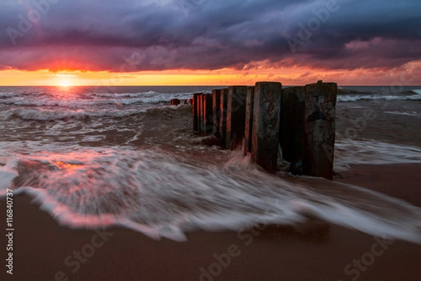 Obraz Right before sunset, the sun came out from the clouds. Its rays highlight the low ?umulus. Last sunbeams put colored gleams on the breakwater and on the waves of the Baltic Sea, Russia, Curonian Spit