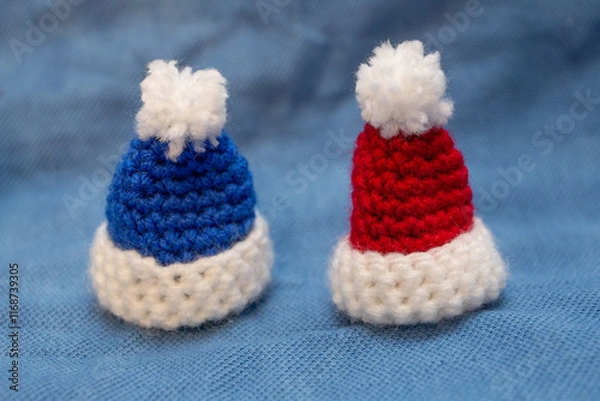 Fototapeta Knitted caps of blue and red color with pom-poms for a soft toy on a blue background.