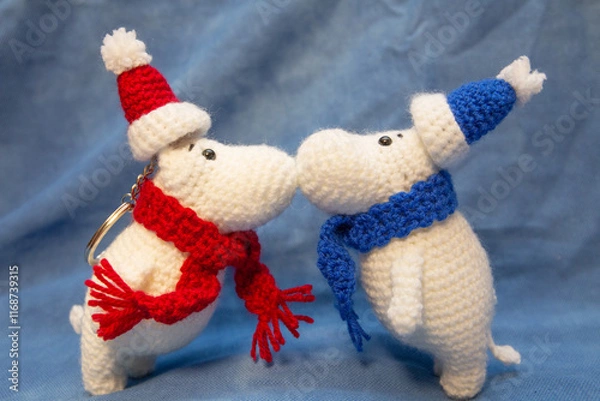 Fototapeta Hand-knitted soft toys, animals in a New Year's blue and red hat, stand with their noses facing each other.
