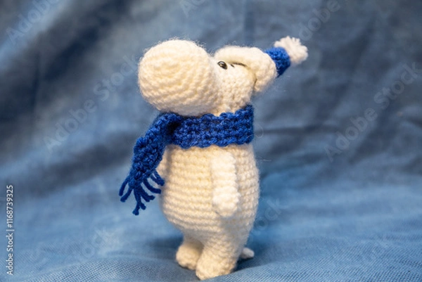 Fototapeta A soft toy in a hat with a pom-pom, a hand-knitted animal in a New Year's blue hat, stands on a blue background.