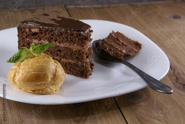 Fototapeta Dessert on a plate on a rustic wooden table: profiterole, decorated with mint leaves and a slice of chocolate cake