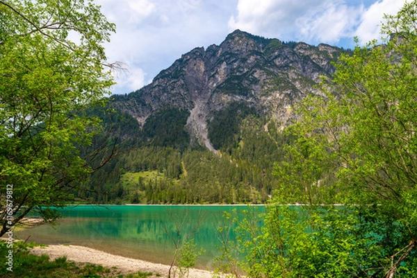Obraz View over the turquoise colored Heiterwanger lake on a sunny day. The mountains are reflected in the smooth water of the lake. Heiterwang, Austria
