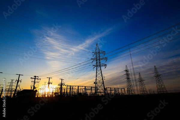 Fototapeta Many high-voltage power towers, silhouetted against the setting sun