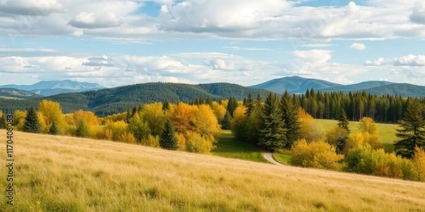 Fototapeta Serene autumnal landscape featuring a winding path through golden foliage and a backdrop of majestic mountains under a partly cloudy sky