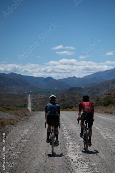 Fototapeta Two friends cycling down a long gravel road in the wilderness during a bicycle riding adventure in vast open spaces.