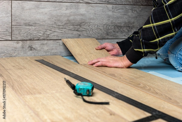 Fototapeta Worker installing laminate flooring in apartment under renovation.