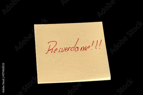 Fototapeta Yellow adhesive paper, similar to a Post-it note, on a black background with the words “Recuerdame in Spanish and three exclamation marks handwritten in red ink.