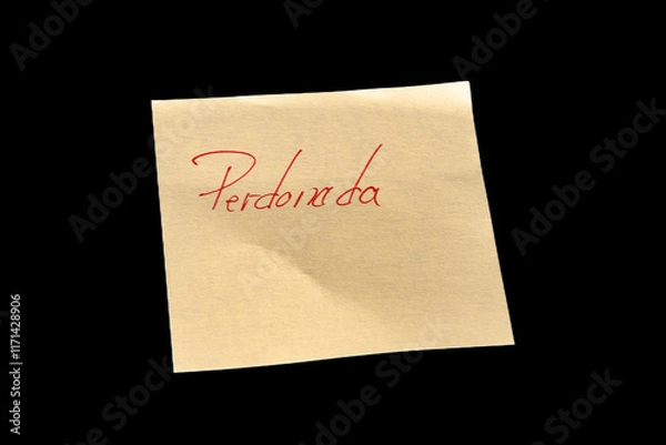 Fototapeta Yellow adhesive paper, similar to a Post-it note, on a black background with the words in Spanish “Perdonada” and  handwritten in red ink.