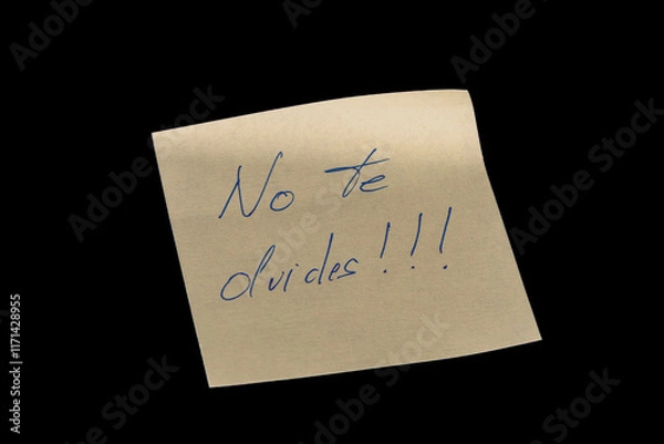 Fototapeta Yellow adhesive paper, similar to a Post-it note, on a black background with the words “No te olvides” in Spanish handwritten in blue ink.