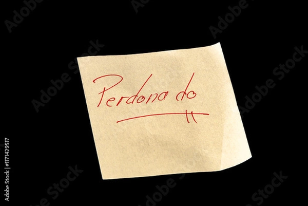 Fototapeta Yellow adhesive paper, similar to a Post-it note, on a black background with the words “Perdonado” in Spanish handwritten in red ink.